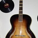 Akustická kytara s polodubovou konstrukcí v tmavě hnědém sunburst provedení. Na těle jsou viditelné dva f-otvory a kovový most. Na hlavě nástroje je…