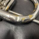 Detail stříbrného mosazného nástroje s viditelnými mechanickými poškozeními. Povrch je v několika místech výrazně odřený, s viditelnými žlutými skvrn…