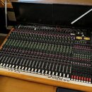 Velký míchací pult s dřevěným rámem a černým ovládacím panelem. Na pravé straně je nápis TOFT AUDIO CONSOLE MTO a logo Toft Audio Design. Panel obsah…