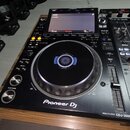 Černý DJský přehrávač s nápisem Pioneer Dj a označením MULTI PLAYER CDJ-3000. Zařízení má velký ovládací jog s modrým podsvícením uprostřed a displej…