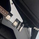 Černá elektrická kytara s bílým pickguardem, položená v černém kufru. Nástroj má dva humbuckery a tři ovládací knoflíky. Na kytáře nejsou viditelné ž…
