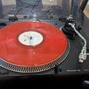 Černý gramofon značky Pioneer DJ s nápisem DIRECT DRIVE TURNTABLE PLX-500. Na talíři je položena červená vinylová deska s bílým středovým štítkem. Př…
