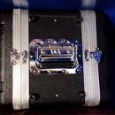 Černý transportní kufr s texturovaným povrchem. Má dvě stříbrné hliníkové lišty a centrální chromovanou rukojeť s připojeným zámkem. Na stranách jsou…