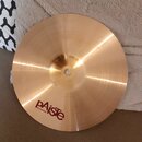 Zlatavý kovový činel s jemným rýhováním povrchu. Na spodní straně je červeným písmem nápis pAiste a pod ním menší text MADE IN SWITZERLAND. V horní č…