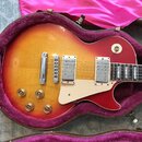 Elektrická kytara s tónem sunburst (červená a žlutá) v hnědém kufru s fialovou výstýlkou. Nástroj má dva humbuckery, čtyři zlaté ovládací knoflíky a…