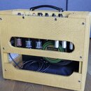 Žlutý kytarový zesilovač v texturovaném potahu s černou rukojetí. V otevřené zadní části jsou vidět elektronické lampy a reproduktor s nápisem CELEST…