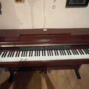Digitální piano v tmavě hnědém dřevěném provedení s bílými a černými klávesami. Nad klaviaturou se nachází ovládací panel s červeným digitálním displ…