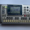Šedý digitální sekvenátor s displejem a množstvím tlačítek. Na horní straně je logo YAMAHA a pod displejem nápisy MUSIC SEQUENCER QY100. V levé části…