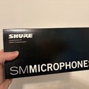 Černá obdélníková krabice s bílými nápisy. V horní části je logo SHURE a pod ním text LEGENDARY PERFORMANCE™. Ve spodní části je velkým písmem napsán…