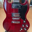 Červená elektrická kytara s černým pickguardem a hnedým hmatníkem. Nástroj má dva humbuckery, čtyři ovládací knoflíky a jeden přepínač. Na kytáře nej…