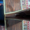Detail zadní strany akustické kytary s tmavým dřevěným povrchem a výraznou sletou. Kolem těla i krku je vidět světlý lem. Povrch lakovaného dřeva vyk…