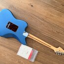 Modrá elektrická kytara zobrazená zbylem. Na zadní straně těla je tmavý hnědý kryt elektroniky a na hlavě hředu je viditelné logo Fender. Vedle nástr…