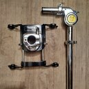 Na fotografii jsou dvě části chromovaného a černého kovového držáku na bubny. Na levé části je nápis OptiMount SUSPENSION SYSTEM a logo Pearl. Pravá…