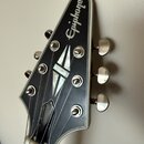 Hlava kytary v černé barvě s bílým lemováním. Na horní části je bílý nápis Epiphone a uprostřed je umístěna vložka s motivem kříže. Jsou zde vidět še…