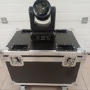 Černý světelný efekt typu moving head umístěný na černé transportní bedně s hliníkovými hranami a úchyty. Na zadním panelu efektu je viditelný disple…