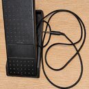 Černý sustain pedál z plastu s protiskluzovou texturou v podobě malých výstupků. Uprostřed je vidět nápis YAMAHA. K pedálu vede černý kabel zakončený…