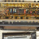 Fotografie zachycuje vnitřek kytarového zesilovače s otevřeným šasi a viditelnými elektronickými komponenty, včetně kondenzátorů a kabeláže. Na předn…