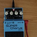 Modrý kytarový efekt s nápisy BOSS, SUPER Chorus a CH-1. Na horní straně jsou čtyři bílé otočné knoflíky s popisky DEPTH, RATE, EQ a E.LEVEL. V levé…