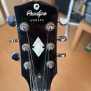 Černá hlava kytary s nápisem Prodipe GUITARS a kulatým logem s písmenem P. Uprostřed je vložena světlá kosočtvercová ozdoba z perlece. Jsou zde vidět…