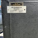 Detailní záběr na černý povrch s texturou kůže, na kterém jsou umístěny dva kovové štítky. Horní mosazný štítek nese nápis Made in the German Democra…