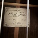 Fotografie zachycuje vnitřní štítek hudebního nástroje. Na bílém podkladu s ozdobným rámem je vyveden nápis Pavel Kriha, rok A.D. 2013 a číslo No. 33…