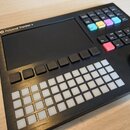 Černý sekvencer Polyend Tracker + s displejem a mřížkou bílých podsvícených tlačítek. V horní části jsou barevné ovládací tlačítka a nápis Polyend Tr…