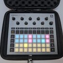 Šedý sampler Novation Circuit Rhythm v černém přepravním pouzdře. Horní část obsahuje osmi otočných ovladačů s popisky jako Master Volume, Start, Sto…