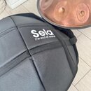 Černý látkový přepravníku s bílým nápisem Sela a pod ním menším textem the soul of sound. Vedle něj je vidět část měděného nástroje s několika vlisov…