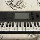 Černý klaviatura MPC s bílými a černými klávesami, umístěná na černém stojanu. Na pravé straně je bílý nápis AKAI PROFESSIONAL a pod ním MPC KEY 61.…