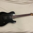 Černá elektrická kytara s tmavým hnedým hmatníkem a světlou dřevěnou hlavou. Na hlavě je viditelné logo Charvel. Kytara má dva humbuckery, jeden ovlá…