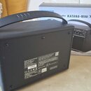 Černý kytarový kombo zesilovač s rukojetí, umístěný vedle původního kartónového obalu. Na krabici je nápis „amplifier KATANA-MINI X“. Na zadní straně…