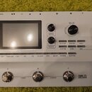 Bílý kytarový efektový procesor s černým pedálem výrazu. Na přístroji je nápis GE250 a text Amp modelling & Multi Effects, v pravé části na pedálu je…