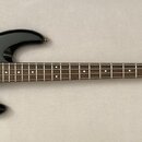 Černá elektrická basová kytara s hnědým hmatníkem a zlatými prvky (kobylka, ladičky). Na hlavě je bílý nápis Fender JAZZ BASS SPECIAL. Nástroj vykazu…