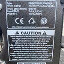 Fotografie detailně zobrazuje dva informační štítky na černém povrchu zařízení. Horní štítkek obsahuje text: Type: OMNITRONIC LS-822A, Power supply:…