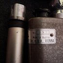 Fotografie zobrazuje dvě stříbrnošedé kovové součástky. Na pravém objektu je bílý štítek s nápisy „Nr: 132“, „Made in Austria“ a „TE Ges. m. b. H., V…