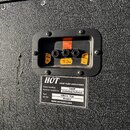 Detail zadní strany černého kytarového boxu s texturovaným povrchem. V horní části je panel se třemi konektory, u kterých jsou žluté papírové štítky…