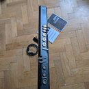 Černý elektronický wind controller s nápisem EWI na horní části. Vedle nástroje leží kabel, dokumentace a šedý obal s nápisem AKAI EWUSB. Nástroj má…