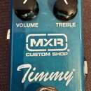 Modrý kytarový efekt s nápisy MXR CUSTOM SHOP a Timmy. Na horní straně jsou čtyři černé otočné knoflíky s popisky VOLUME a TREBLE, přepínač CLIP a st…