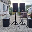 Sada dvou černých aktivních reproduktorů a dvou subwooferů na tripodních stojanech. Na všech čtyřech komponentech je viditelné oranžové logo JBL. Pov…