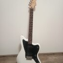 Bílá elektrická kytara s černým plechtrádem a hnědým hmatníkem. Na hlavě je viditelné logo "Stratocaster". Nástroj vykazuje čistý povrch bez viditeln…