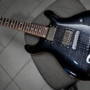 Kytara s tmavě modrým průsvitným lakem a viditelnou strukturou dřeva. Nástroj má dva humbuckery, tři kontrolní knoflíky a přepínač zvuků. Na hmatníku…