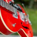 Červená polodublová elektrická kytara s bílým lemováním hran. Na hmatníku je vidět černý pickguard a dva snímače s kovovými kryty. Povrch laku vykazu…