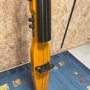Detailní pohled na tělo žlutého elektrického smyčcového nástroje s černým hmatníkem a čtyřmi strunami. Na boku jsou umístěny dva černé ovládací knofl…