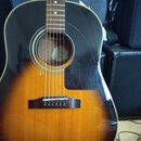 Akustická kytara s tělem v provedení sunburst (přechod od černé k žlutohnaté). Nástroj má tmavý hmatník a černý plechtr zaštitu. Uvnitř otvoru rezona…