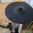 Černý gumový cymbal elektronické bicí s nápisem Roland. Nástroj je umístěn na kovovém stojanu. Povrch cymbalu vykazuje mírné známky opotřebení v podo…