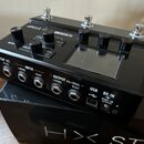 Černý kytarový procesor Line 6 HX Stomp s displejem a čtyřmi ovládacími knoflíky. Na horní straně jsou tři kovové spínače a nápisy STOMP, LINE 6, PAG…