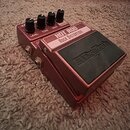 Kytarový efekt pedál v červenohnatém kovovém šasi. Na horní části je bílý nápis HOT ROD ROCK DISTORTION a na černém spínacím tlačítku je vyražené log…