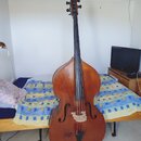 Na fotografii je dřevěný kontrabas v hnědé barvě. Nástroj má standardní tvar s f-otvory a světlým mostkem. Na hlavě nástroje nejsou žádné čitelné náp…
