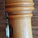 Detail dřevěného nástroje světle hnědé barvy s výraznou masivní vrstvou laku. V horní části jsou vidět tři vyfrézované prsteny a níže se nachází kula…