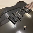 Černá elektrická kytara s lesklým povrchem a hnědým hmatníkem. Nástroj má dva černé humbuckery, černý pickguard a černý kobylník. Na kytáře nejsou vi…